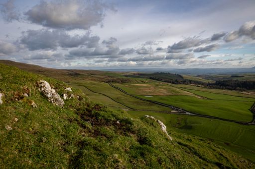 A scenic view of lush green fields and rolling hills under a partly cloudy sky in Skipton