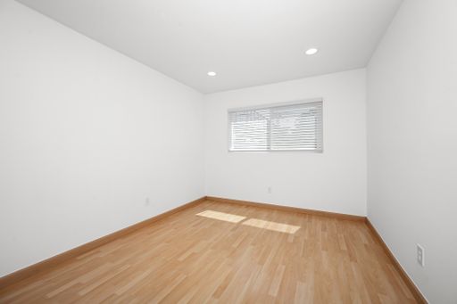 Empty white room with wooden floors and windows, adorned with two blinds