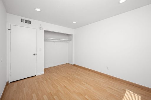 Modern bedroom with white walls, hardwood floors, and multiple closets