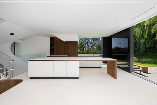 Open plan kitchen with white counter, wooden shelves, and doors
