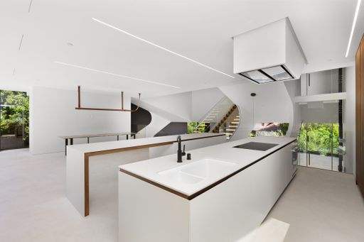 Modern kitchen with white counters and walls, featuring stairs to a second level