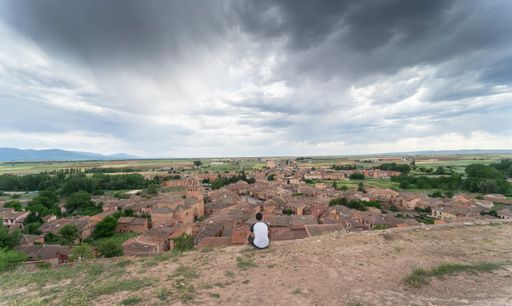 Young man sitting watching life go by while observing the medieval village of Ayllon from the top of a hill on a summer day with cloudy skies.