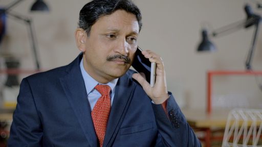 A shallow focus shot of a middle-aged Indian man wearing a suit and talking on his pho