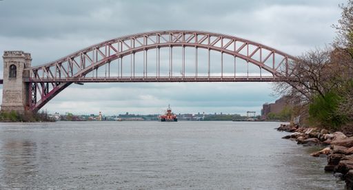 A wide shot of a bridge over water with a boat sailing in the distance in Queens NYC