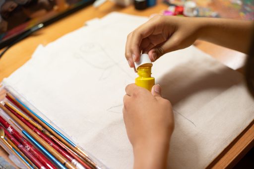 A closeup shot of hands opening the bottle of yellow paint