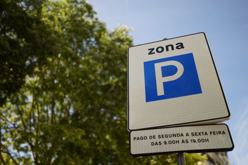 A closeup of a white and blue Portuguese park traffic sign against blurry trees