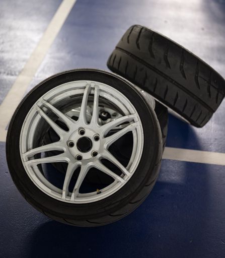 Detail of three sports car wheels stacked on the parking lot floor, white 6-spoke wheels with Semislick tires in vertical format