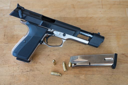 Detail of a nice open and unloaded 9mm police pistol next to a loaded bullet magazine and a few bullets on the wooden table