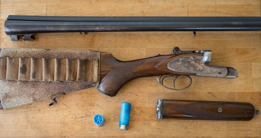 Detail of a beautiful and old disassembled parallel shotgun on a wooden table, there are also some 12 gauge cartridges