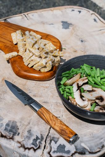 A vertical closeup of a knife on a plate with tempe, mushrooms and beans