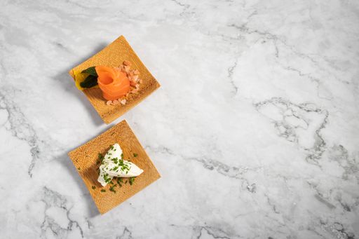 A top view of delicious appetizers on a small wooden plate on a marble texture table
