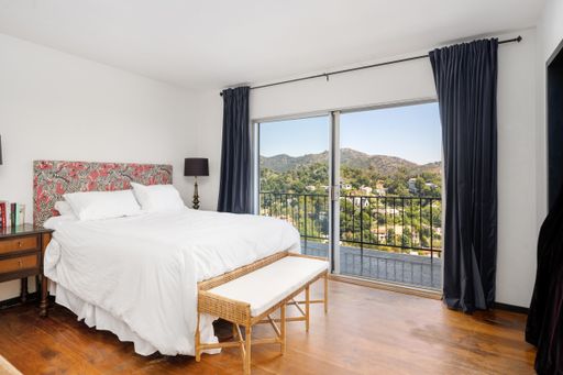 A bedroom with a white bed, wooden floors, and a balcony with a mountain view. Los Angeles, California