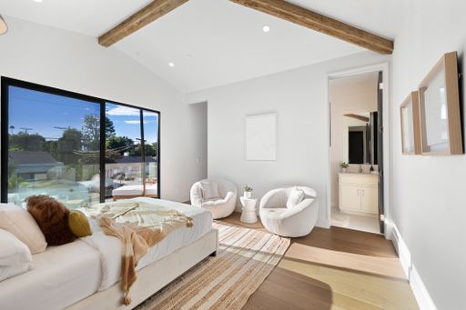 A spacious bedroom with white furnishings and a large wooden beam ceiling