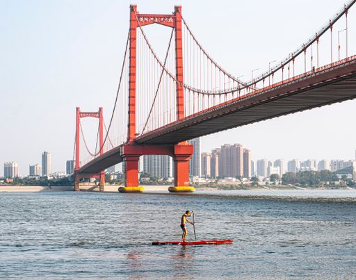The view of Wuhan Yingwuzhou Bridge spanning the Yangtze River with an athlete rowing a kayak by the bridge
