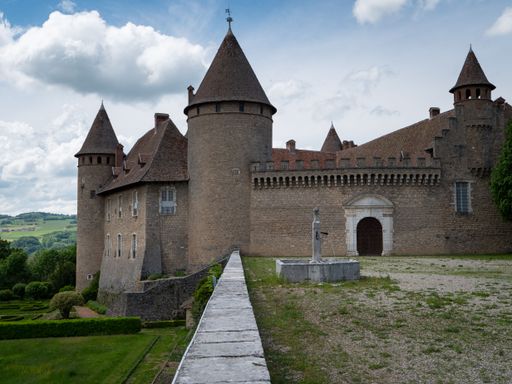 A medieval castle with conical towers and a stone courtyard on a sunny day in the countryside.
