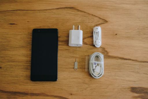 A top view of a brand new black smartphone with a charger and earphones on a wooden table