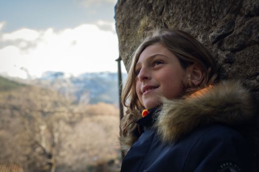 A young boy in a winter coat smiling and leaning against a stone wall.