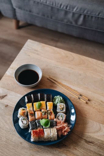 A vertical shot of a plate of assorted sushi on a wooden table next to soy sauce and chopsticks