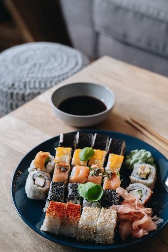 A vertical shot of a plate of assorted sushi on a wooden table next to soy sauce and chopsticks