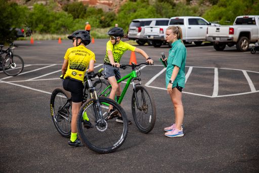 The young cyclists in yellow jerseys talking to a coach in a parking lot before a race.