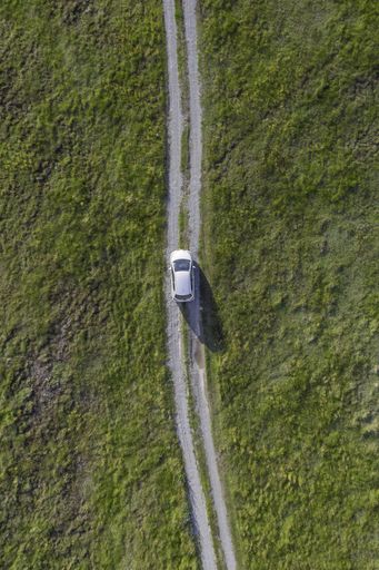 A vertical high angle shot of a white car riding through the path in the green valley