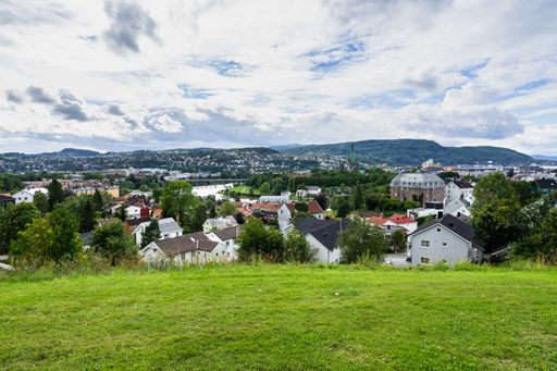 A landscape of Trondheim surrounded by hills covered in greenery under a cloudy sky in Norway