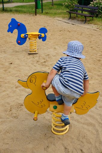 A young male ki climbing on a wooden duck ride at a playground in the Orla Bialego area