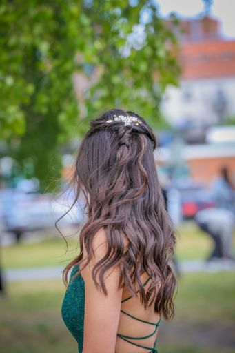 A young woman with long wavy hair in an elegant green dress with a hair accessory, standing outdoors. The prom in Ludvika, Sweden. Vertical shot.