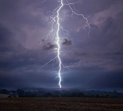 A dramatic lightning bolt striking down during a thunderstorm over a rural landscape. Lewisburg