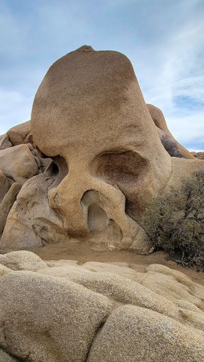 A close-up view of Skull Rock in Joshua Tree National Park under a partly cloudy sky