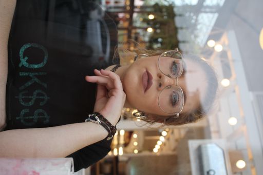 A portrait of a young beautiful Spanish woman with glasses looking at the camera from behind the glass