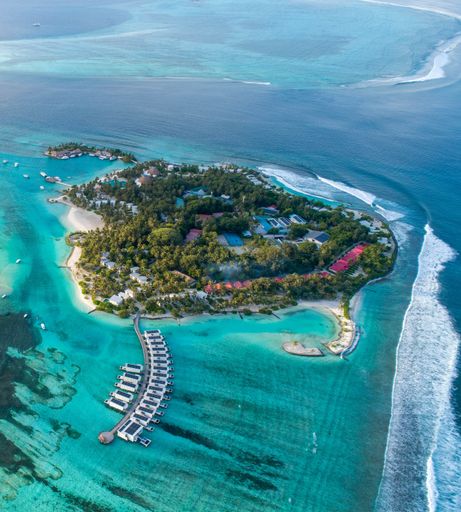 An aerial view of a tropical island with clear turquoise waters and overwater bungalows in the Maldives