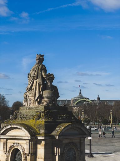 A statue in Place de la Concorde with Grand Palais in the background on a clear day in Paris, France.
