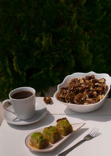 A cup of coffee with baklava and a cup of coffee on a white table outdoors