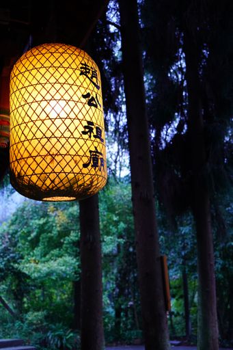 A traditional Japanese lantern hanging in a forested area during twilight