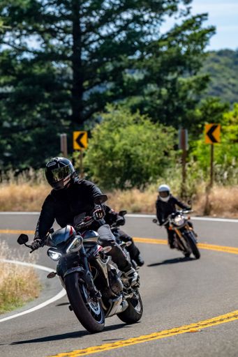 A group of motorcyclists riding on a scenic winding road through a forested area