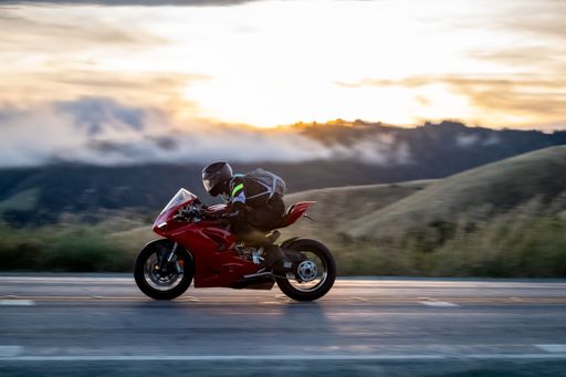 Motorcyclist riding a red sports bike at high speed on a scenic mountain road at sunset