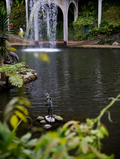 A tranquil garden scene featuring a statue in a pond, with a waterfall and lush greenery in the background.