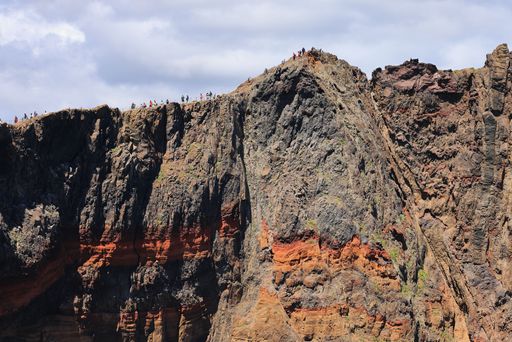A group of hikers walking on the edge of a rugged mountain in Vereda da Ponta de Sao Lourenco, Madeira, Portugal on a sunny day