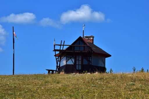 A small wooden hut in the Bulgarian countryside, in the Dobrostan area, Eastern Europe. Surrounded by short dry yellow grass and with blue sky.