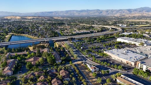 Aerial view of a suburban area with a highway, residential buildings, and a small lake in San Jose, California with mountains in the background.