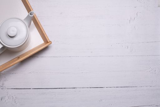 A high angle shot of a white teapot on a tray on a white wooden table