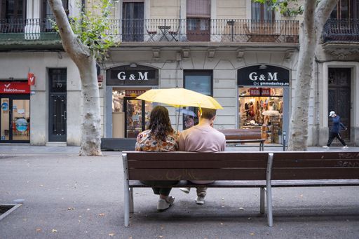 A young couple sitting on a bench under a yellow umbrella at Rambla del Poblenou, Barcelona, Spain