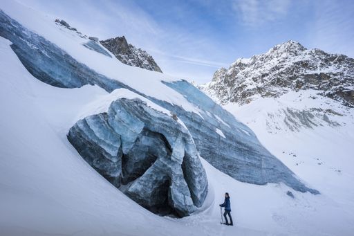 Winter landscape view of a snowshoes' hiker in front of a collapsed ice cave partially covered by snow