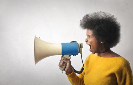 A beautiful young black woman looking yelling with a megaphone against a white wall