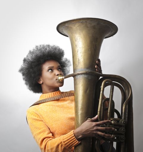 A portrait of a young black woman with short curly hair playing the tuba