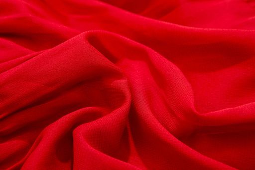 A close-up of vibrant red fabric with soft folds and texture
