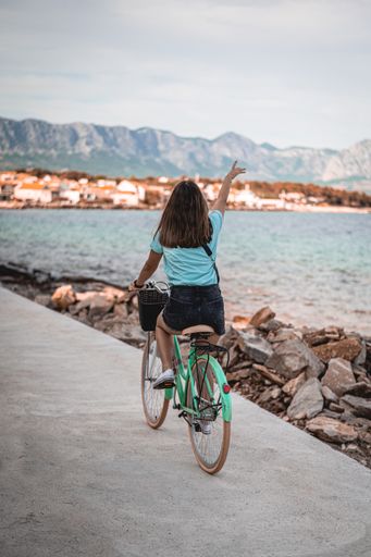A back of a female riding a bicycle on a concrete road near the bay