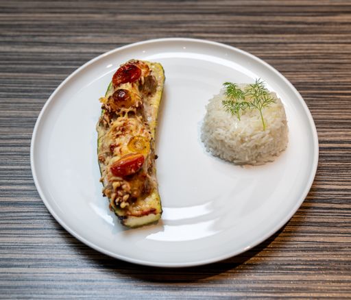 A closeup shot of an aubergine stuffed with tomatoes and cheese on a white plate with rice side dish