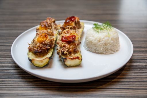 A closeup shot of aubergines stuffed with tomatoes and cheese on a white plate with rice side dish